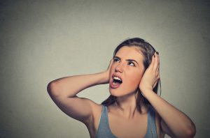 Closeup portrait young unhappy stressed woman covering her ears looking up stop making loud noise it's giving me headache isolated on gray wall background. Negative emotion face expression feeling